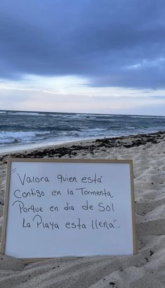 a sign that is on the sand by the ocean with writing in spanish and english