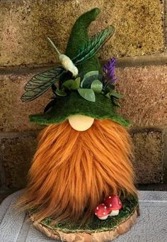 an odd looking hat with long hair and green leaves on the top, sitting on a piece of wood