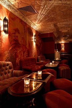 a dimly lit room with couches, tables and lamps on the ceiling is decorated in an art deco style