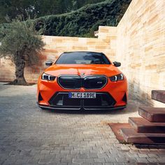 an orange car parked in front of a brick wall and steps with trees behind it