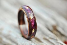 a wooden ring with purple and gold inlays sitting on top of a piece of wood