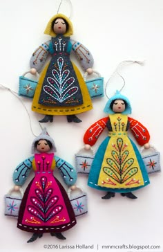 three christmas ornaments in the shape of people wearing colorful dresses and holding presents, on a white background