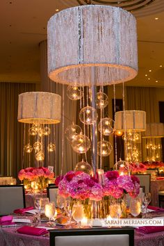 a chandelier hanging from the ceiling over a table with pink flowers and candles