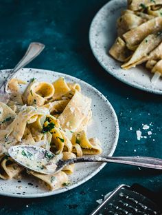 two plates of pasta with parmesan cheese on them and a fork next to it