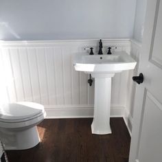 a white toilet sitting next to a sink in a bathroom on top of a hard wood floor