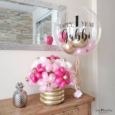 a vase filled with pink and white balloons on top of a wooden table next to a mirror