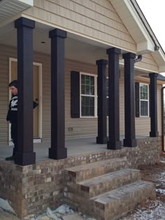 a man standing on the front porch of a house with black pillars and brick steps