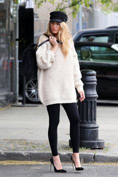 a woman is standing on the street talking on her cell phone while wearing black leggings and a white sweater