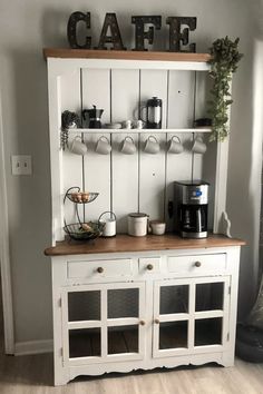 a white hutch with coffee maker and cups on the top, next to a wooden sign that says cafe