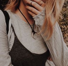 a woman with long blonde hair wearing a black and grey shirt holding her hands to her face