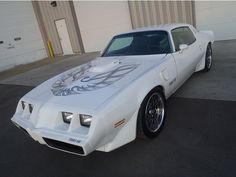 a white car parked in front of a garage with an artistic design on the hood