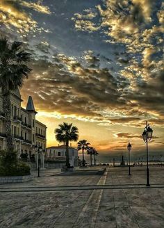 the sun is setting over an empty city square with palm trees and buildings in the background