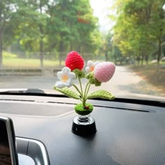 three crocheted flowers in a vase sitting on the dashboard of a car,