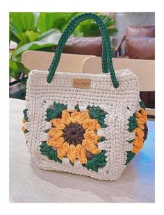 a crocheted bag with sunflowers on the front and green handles sitting on a table