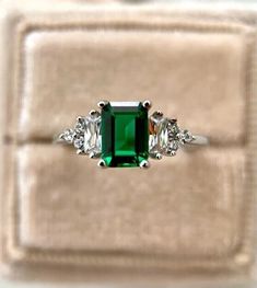 an emerald and diamond ring with three diamonds on it's side, sitting in a velvet box