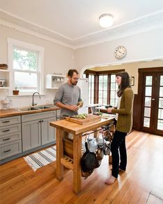 a man and woman standing in a kitchen next to a table with pots on it