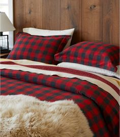 a bed with red and black plaid comforter next to a lamp on a wooden headboard