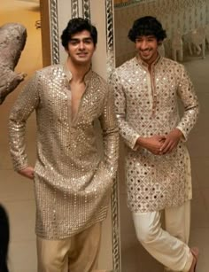 two men standing next to each other in front of a mirror wearing gold and white outfits