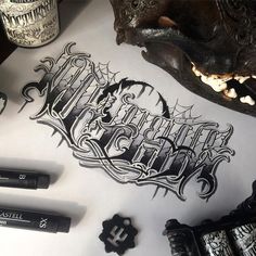 some type of lettering on top of a white paper next to ink pens and markers