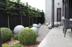 an outdoor patio area with stone balls and shrubbery on the side of the house