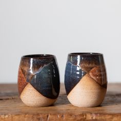 two cups sitting on top of a wooden table next to each other, one with an abstract design