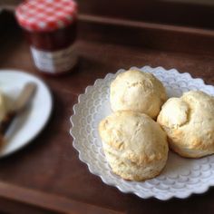 three biscuits on a plate next to a cup of coffee and a jar of jam