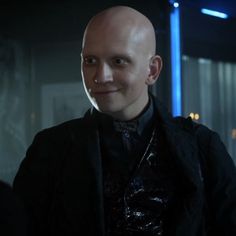 a bald man wearing a black jacket and tie in a dark room with blue lights