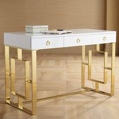 a white and gold desk with two drawers on each side, in front of a wooden floor