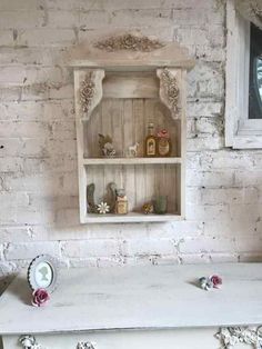 an old white table with some flowers on it and a shelf in the corner next to it