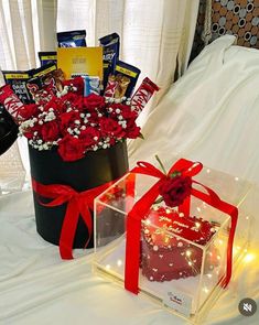 two gift boxes with candy and flowers in them on a white tablecloth covered bed