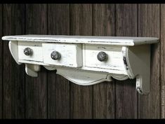 an old white wall mounted shelf with three knobs and two drawers on the bottom