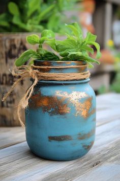 a blue mason jar filled with green plants on top of a wooden table next to a potted plant