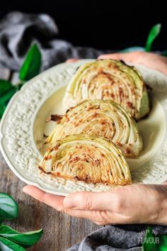 two hands holding a plate with sliced cabbage on it and green leaves in the background