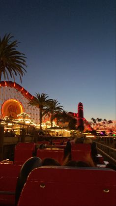 an amusement park at night with people riding on the rides and palm trees in the background