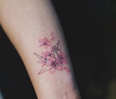 a small tattoo on the wrist of a woman with pink flowers and an origami