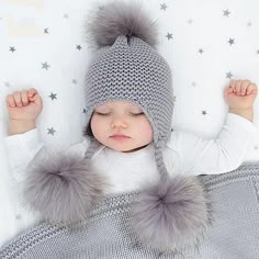 a baby wearing a knitted hat with two pompoms