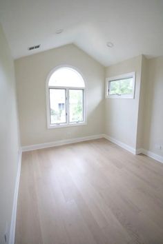 an empty room with wood floors and two windows in the corner, looking into another room