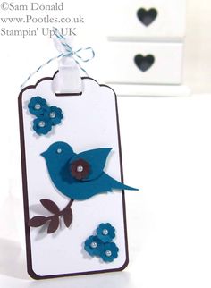 a blue bird on a white tag with flowers and hearts in the background, hanging from a string