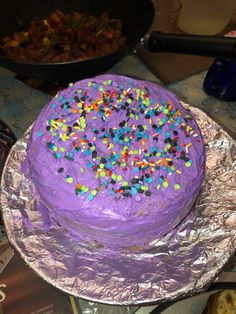 a purple frosted cake with sprinkles on it sitting on tin foil