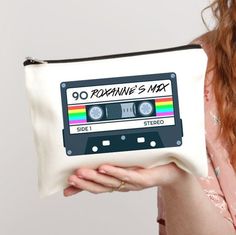 a woman holding a white zippered pouch with an old school cassette tape design