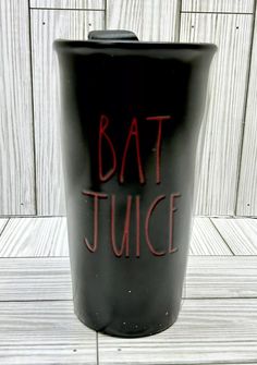 a black cup with the words bat juice on it sitting on a wooden floor next to a wall