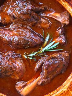 some meat and sauce in a bowl with a sprig of rosemary