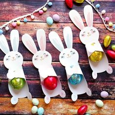 three paper bunnies with easter eggs in them and some bunny decorations on the table