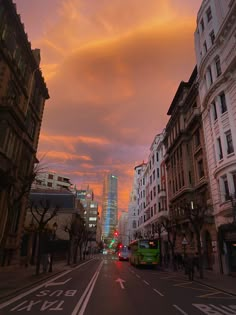 a city street at sunset with buildings and cars on the road in the foreground