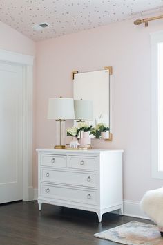 a white dresser sitting next to a window in a room with pink walls and wooden floors