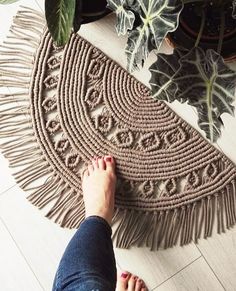 a person standing on the floor next to a potted plant and rug with fringes