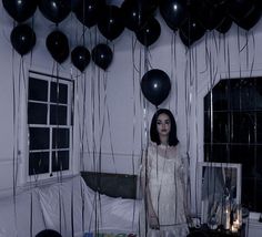 a woman standing next to a bed with black balloons hanging from it's ceiling