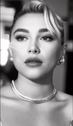 a black and white photo of a woman with short blonde hair wearing a pearl necklace