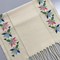 a white table cloth with colorful flowers and fringes on the edge, sitting on a gray surface