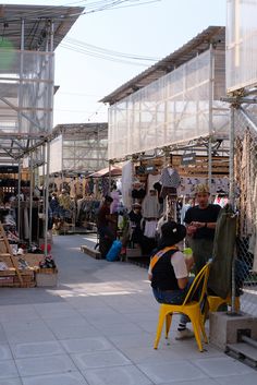 two people sitting at a yellow chair in front of an open market with lots of items